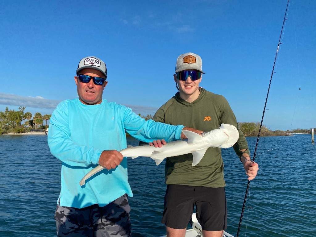 Two anglers with a small hammerhead shark on a boat